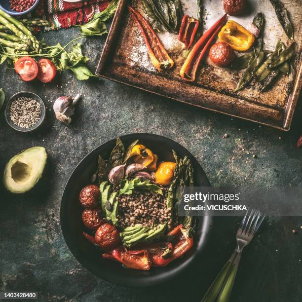 healthy food bowl with grilled and roasted vegetables, avocado and quinoa at rustic kitchen table with ingredients and kitchen utensils - buddha bowl stockfoto's en -beelden