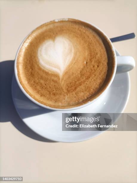 high angle view of coffee cup with heart shaped latte art on table - coffee art stockfoto's en -beelden