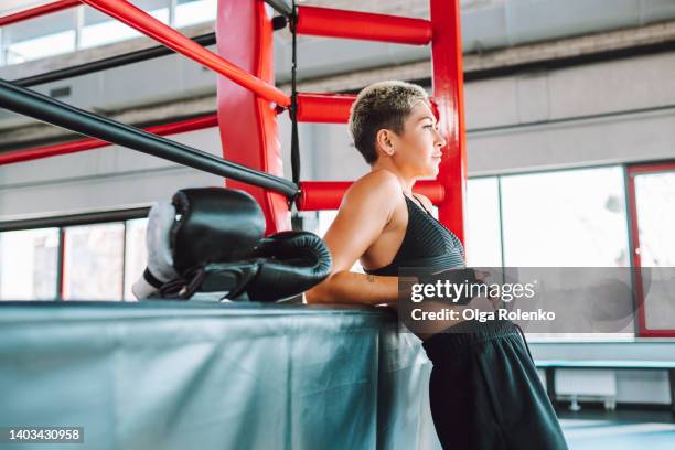 a brutal middle-aged woman with a very short haircut is resting in a boxing gym in a sports uniform, side view - brutal womens boxing foto e immagini stock