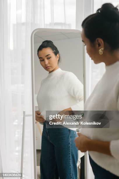 asian woman standing in front of mirror wearing a casual clothes - preocupación por el cuerpo fotografías e imágenes de stock