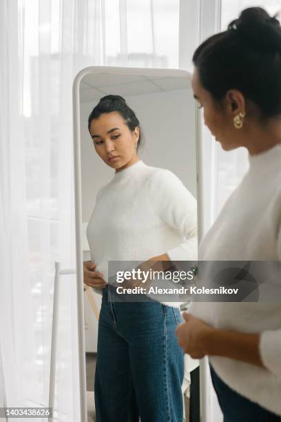 asian woman standing in front of mirror wearing a casual clothes - weight gain stockfoto's en -beelden