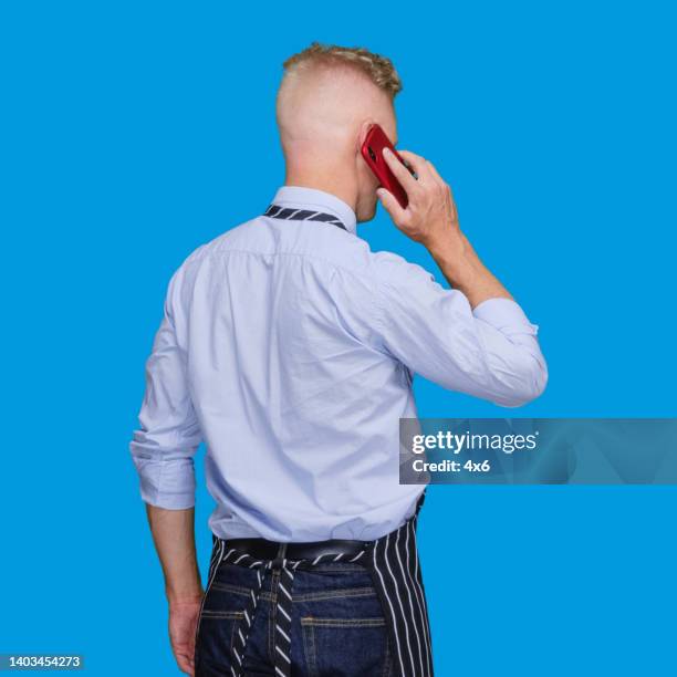 caucasian male butcher standing in front of blue background wearing button down shirt and using mobile phone - blue shirt back stock pictures, royalty-free photos & images