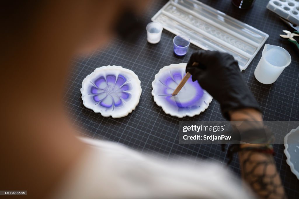 Mujer artesana vertiendo epoxi en el molde de silicona, mientras trabaja desde su taller casero