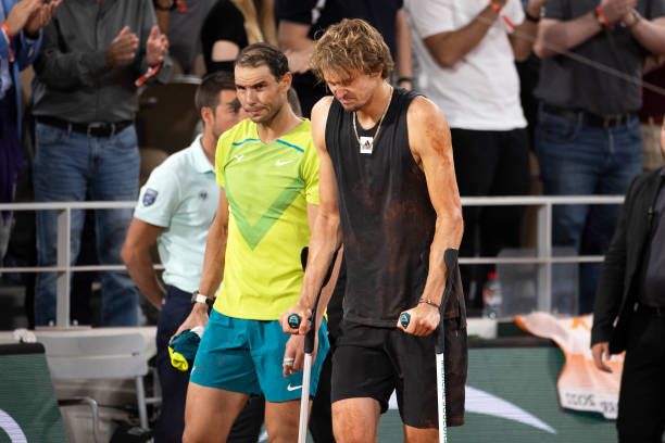 An injured Alexander Zverev of Germany returns to the court on crutches to retire accompanied by Rafael Nadal of Spain after injuring his ankle...