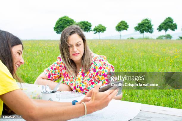 two young women having picnic at table in public park - garden table stock pictures, royalty-free photos & images