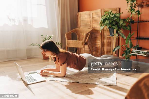 sporty plus size woman in sportswear working out at home, doing plank on yoga mat in front of open laptop, repeating instructions by professional fitness trainer watching online video tutorial - plus size women stock-fotos und bilder