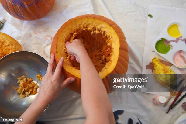 woman decorating a jack-o-lantern pumpkin, taking seeds out of the inside of the pumpkin - schnitzen stock-fotos und bilder