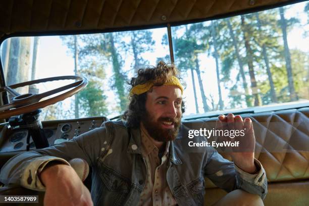 man sitting on floor next to drivers seat on an old retro tour bus, with denim jacket and yellow bandana - headband stock-fotos und bilder