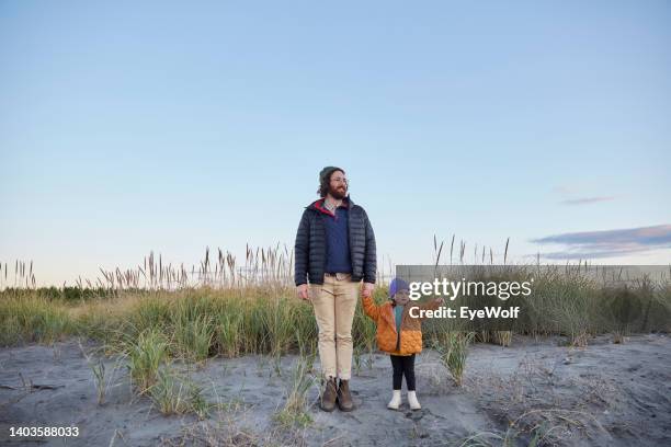 a young father with his daughter holding hands at the beach and looking off at the ocean - beach wide stock pictures, royalty-free photos & images