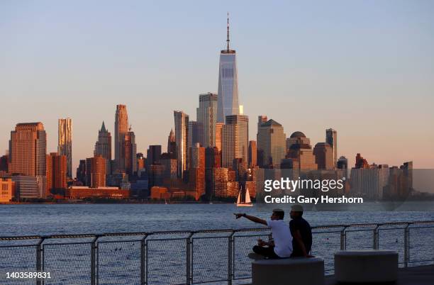 The sun sets on the skyline of lower Manhattan and One World Trade Center in New York City as people sit next to the Hudson River on June 17 in...