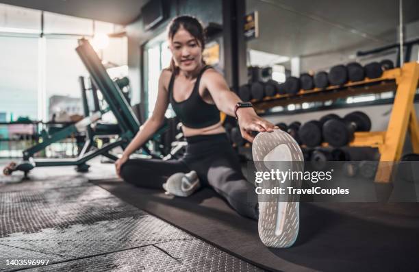 smiling healthy fitness woman sitting on floor stretching leg. gym girl athlete stretch and prepare body for workout. sport and recreation - leg stretch girl stock-fotos und bilder