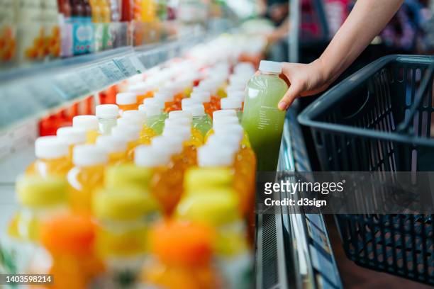 cropped shot of young asian woman shopping for fresh fruit juice from refrigerated shelves in supermarket, taking out a bottle of freshly squeezed green juice into a shopping basket. healthy eating, go green lifestyle - shoppers ahead of consumer price index stockfoto's en -beelden