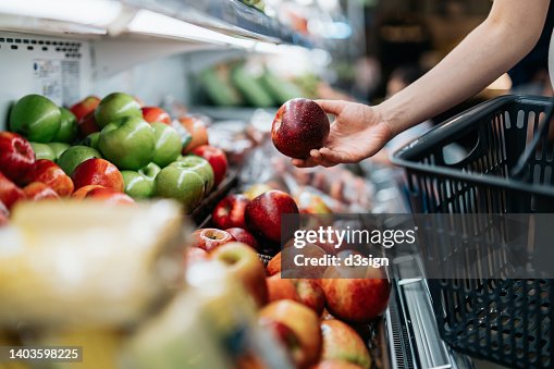 Cropped shot of young Asian woman choosing fresh organic fruits in supermarket. She is picking a red apple along the produce aisle. Routine grocery shopping. Healthy living and eating lifestyle Cropped shot of young Asian woman choosing fresh organic fruits in supermarket. She is picking a red apple along the produce aisle. Routine grocery shopping. Healthy living and eating lifestyle