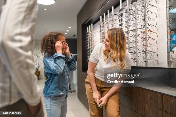 black girl and female optician looking at each other - photo store stock pictures, royalty-free photos & images