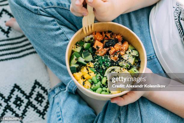 girl in jeans holding salmon poke bowl with mango, cucumber, avocado, salmon fish, rice, asian bowl, edamame beans, chukka, ginger, nori, sesame, lime. top view - bowl of cereal stock pictures, royalty-free photos & images