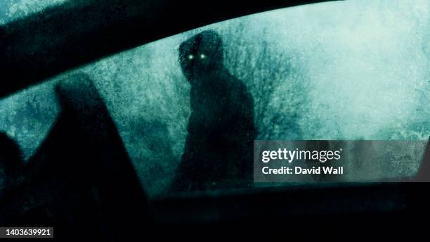 a horror concept of a spooky supernatural figure with glowing eyes. looking into a car window on a stormy winters evening. with a blurred, textured edit. - demon fotografías e imágenes de stock