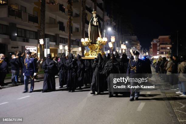 Italian guards of honor wearing COVID-19 protective facial masks walk along with hooded men dressed in black robes carrying torches and the statuette...