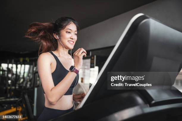 woman running in a gym on a treadmill concept for exercising. fitness and healthy lifestyle. girl running on the treadmill and listening to music at the gym - treadmill fotografías e imágenes de stock