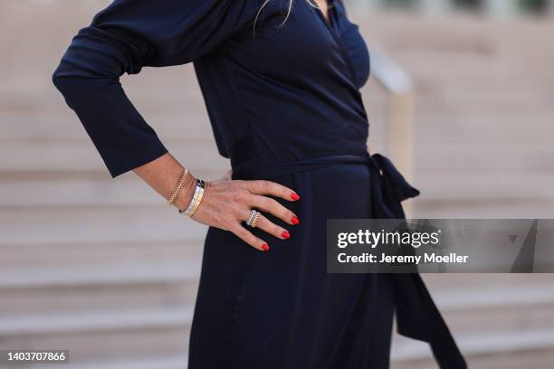 Sue Giers seen wearing a dark blue silk midi dress from SoSue, a golden Clash De Cartier bracelet, silver and golden Cartier Love bracelets, silver...