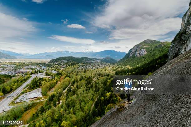a man hangs at belay station on the stawamus chief while rock climbing - belaying stock pictures, royalty-free photos & images