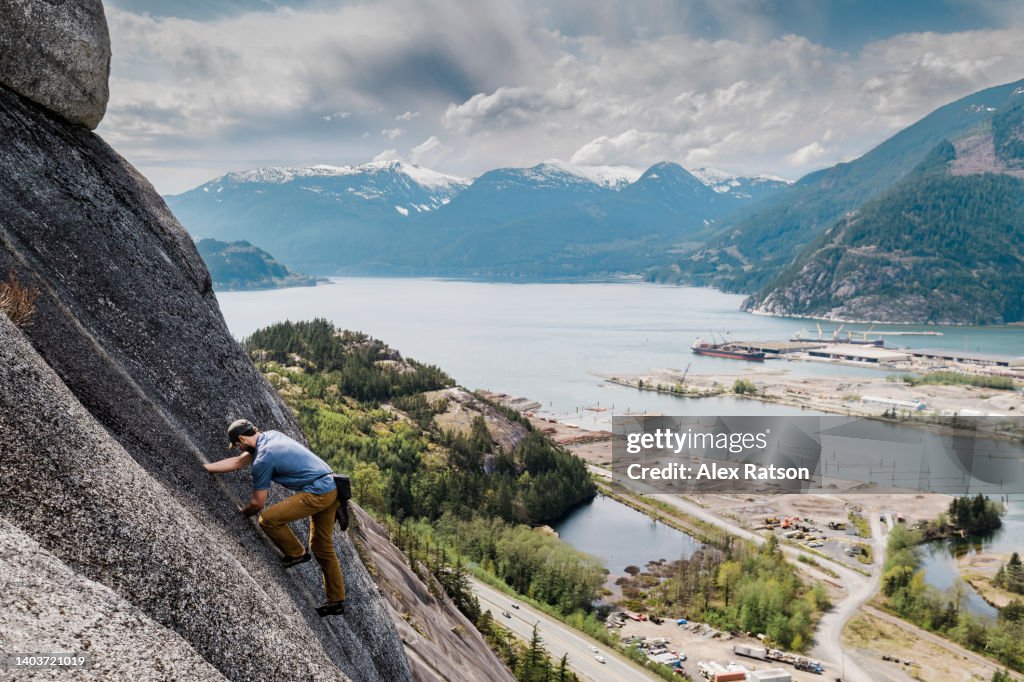 A man free solo rock climbs on the Stawamus Chief with a fjord in the background