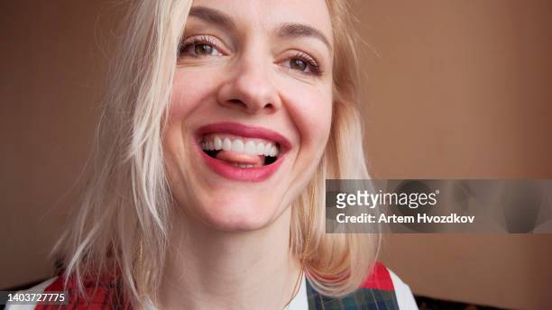 laughing-seductive blonde woman, dressed in red-green colored vest. clean brown colored, wall background - extreme close up mouth stock pictures, royalty-free photos & images