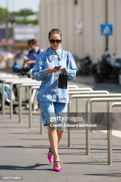 Jenny Nelly wears sunglasses, a blue denim shirt with puff ruffle sleeves and a Peter Pan collar and printed clouds, slit mini blue denim shorts with...
