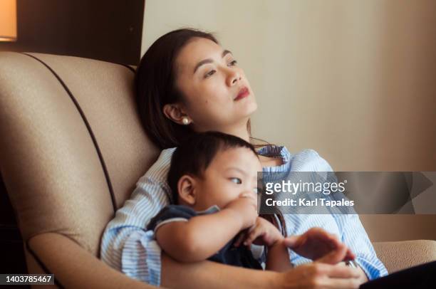 candid portrait of a depressed southeast asian mother in the living room with her son - southeast asia stock-fotos und bilder