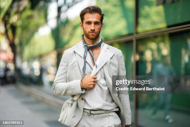 Daniel Toni Jais wears a dark gray and beige print pattern silk small scarf, a pale gray linen blazer jacket, matching pale gray linen suit pants, a...