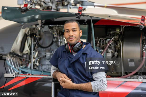 handsome african american aviation engineer standing near helicopter, front view - vliegtuigmonteur stockfoto's en -beelden