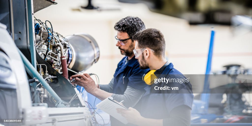 Mécanicien d’aviation enseignant collègue examinant le moteur, vue de côté