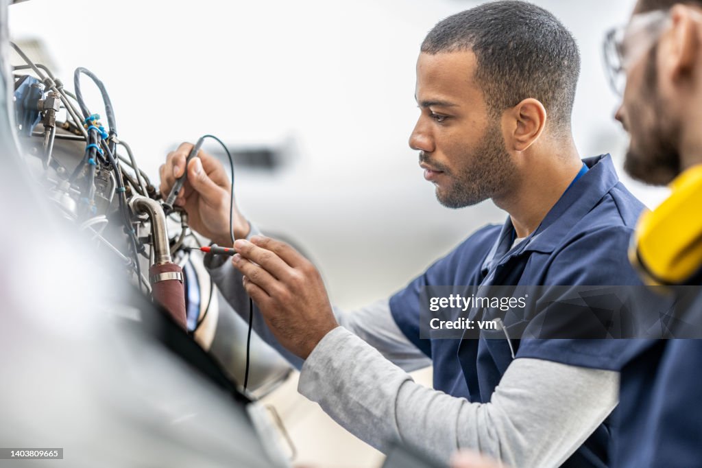Aircraft engineers examining helicopter engine with multimeter, close up