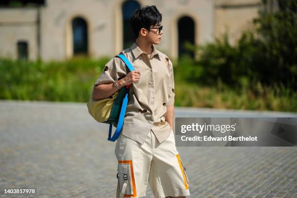 Guest wears glasses, a gold chain necklace, a beige oversized / short sleeves shirt with cut-out heart pattern, white latte with yellow details...