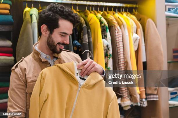 smiling male customer holding hoodie in store - sportswear retail stock pictures, royalty-free photos & images