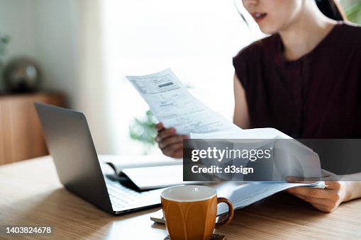 Cropped shot of Asian woman sitting at dining table, handling personal finance with laptop. She is making financial plan and planning budget as she go through her financial bills, tax and expenses at home. Wealth management, banking and finance concept Cropped shot of Asian woman sitting at dining table, handling personal finance with laptop. She is making financial plan and planning budget as she go through her financial bills, tax and expenses at home. Wealth management, banking and finance concept