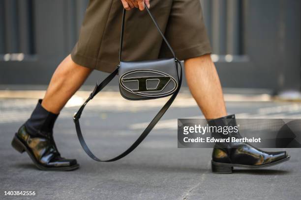 Guest wears a dark khaki short sleeves / belted /buttoned / short jumpsuit, a black shiny leather with gold oversized logo handbag from Diesel, black...