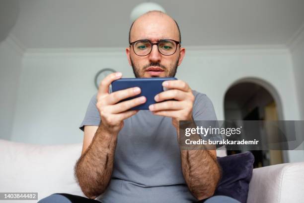 jeune homme jouer à des jeux vidéo sur son smartphone - jeu mobile photos et images de collection