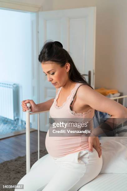 pregnant woman with labor pain, sitting on a bed - employment and labour 個照片及圖片檔