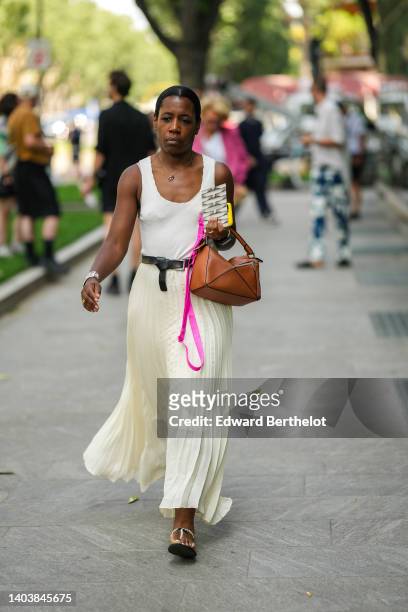 Guest wears a gold chain pendant necklace, a white tank-top, a black shiny leather belt, a camel shiny leather Puzzle handbag from Loewe, a white...