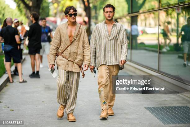 Guest wears black sunglasses, a beige oversized linen shirt, a brown crossbody bag, beige and dark brown striped print pattern large pants, camel...