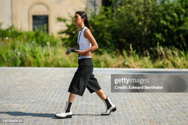 Guest wears a white ribbed cropped tank-top, black large shorts, white leather ankle boots, a green shiny leather long necklace, outside the MSGM...