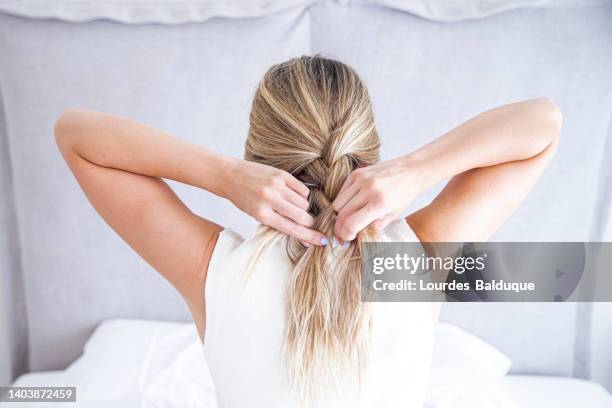 woman fixing hair in her room, seen from behind - braids stockfoto's en -beelden