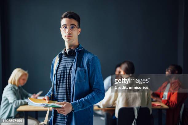 portrait of handsome male student holding notebooks while standing in the library - male student wearing glasses with friends stockfoto's en -beelden