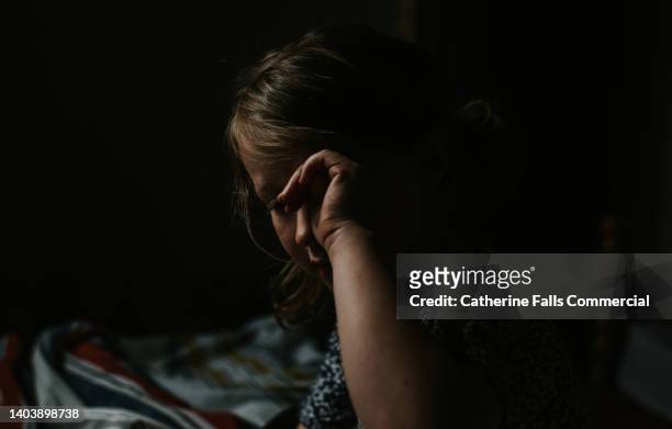 a dreamy, shadowy image of a little girl rubbing her eyes in a dark room - beds dreaming children stock pictures, royalty-free photos & images