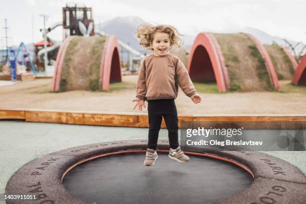 funny and happy curly child jumping on a trampoline. positive emotions and laugh - jumping girl stock-fotos und bilder