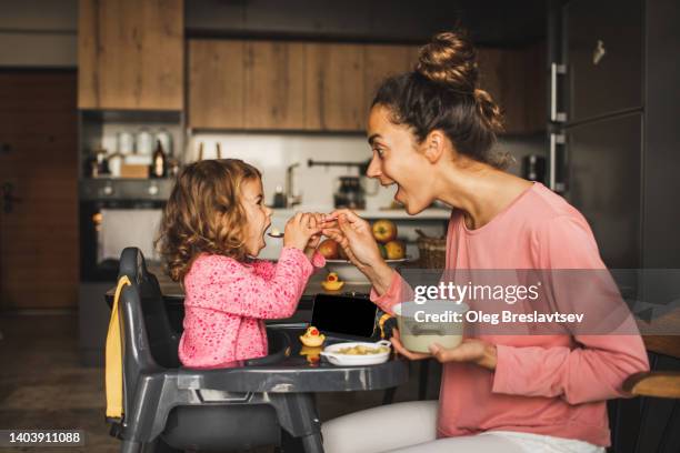 mother feeding little baby daughter and both having fun and laughing. harmony in family - rest home stock-fotos und bilder