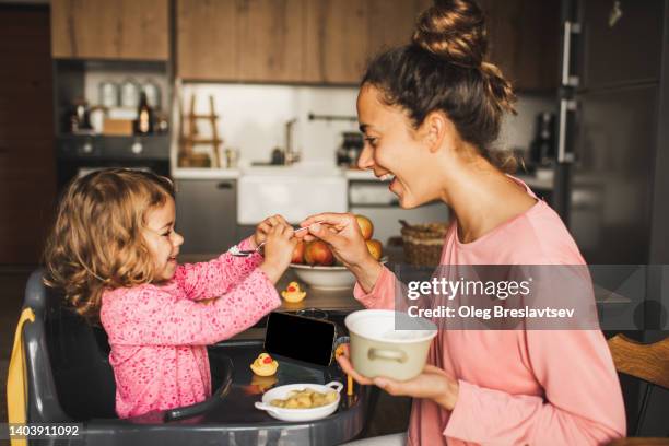 mother feeding little baby daughter and both having fun and laughing. harmony in family - rest home stock-fotos und bilder