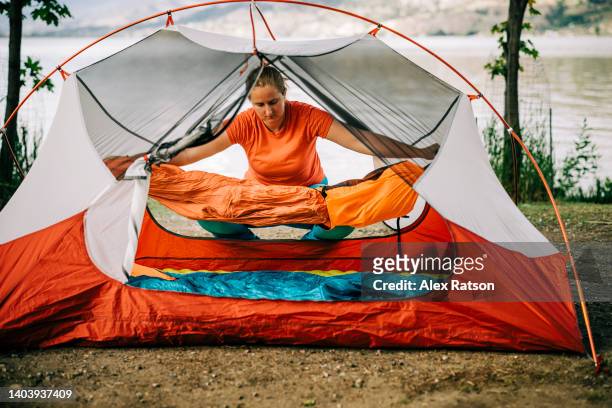 a woman lays out a sleeping bag inside a tent at a campground - sleeping bag stock pictures, royalty-free photos & images