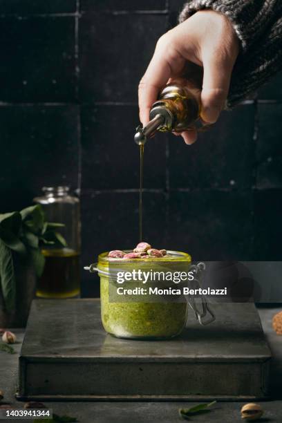 sage and pistacchio pesto in glass jar, human hand - pouring sauce stock pictures, royalty-free photos & images