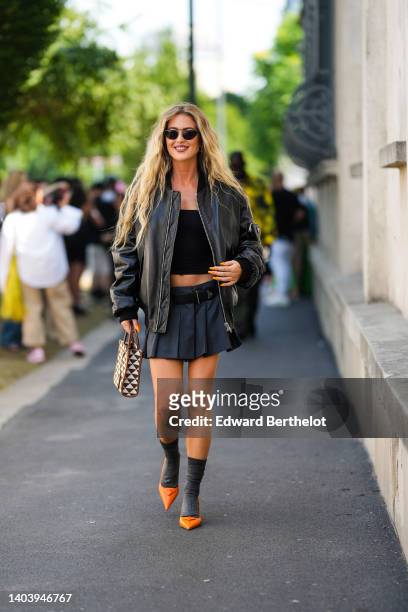 Emili Sindlev wears black sunglasses, a black shiny leather oversized bomber coat from Prada, a black shoulder-off cropped top, a dark gray pleated...